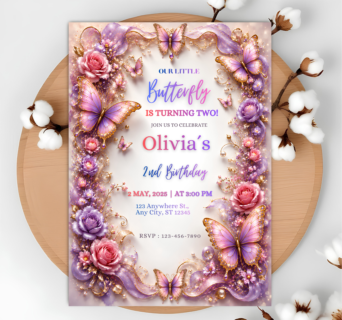 A square butterfly-themed birthday invitation card for 'Olivia's 2nd Birthday' is displayed flat on a round wooden tray, surrounded by cotton bolls. The card features a highly detailed, colorful border of purple and pink butterflies, roses, and gold glitter accents against a light pink background.